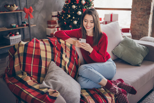 Full body photo of girl sit couch read x-mas news on smartphone in house indoors with christmas advent decoration