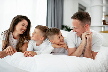 Young family enjoying in bed. Happy parents with sons relaxing in bed