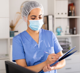 Positive female doctor wearing face mask and blue overall meeting client before consultation