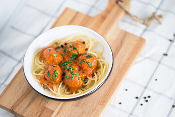 Meatballs in tomato sauce with pasta in the white plate on the coolking cutting board with onion topping and pepper