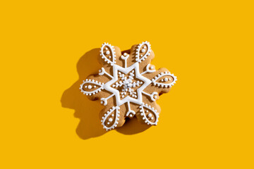 Christmas biscuit. Winter holidays food art. Festive adornment. Beige homemade gingerbread snowflake shape cookie with white icing isolated on orange copy space background.