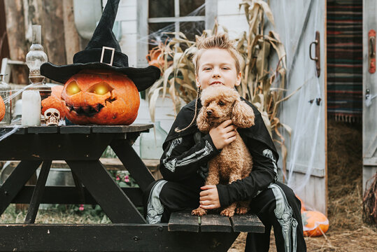 a boy in a skeleton costume with a dog on the porch of a house decorated to celebrate a Halloween party