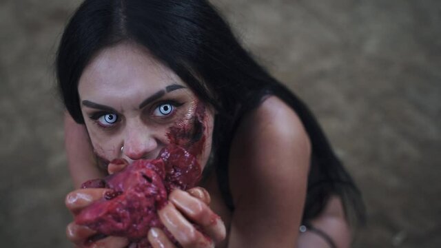 Zombie woman with blue eyes eating raw meat with blood
