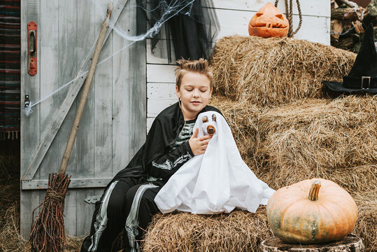 a boy in a skeleton costume with a dog in a ghost costume on the porch of a house decorated to celebrate a Halloween party