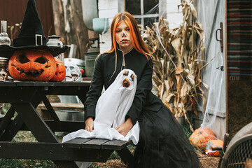 a girl in a witch costume with a dog in a ghost costume having fun on the porch of a house...