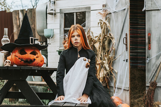 a girl in a witch costume with a dog in a ghost costume having fun on the porch of a house decorated to celebrate a Halloween party
