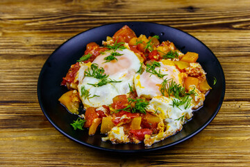Homemade breakfast shakshuka - fried eggs, onion, bell pepper, tomatoes and dill on rustic wooden table. Jewish cuisine