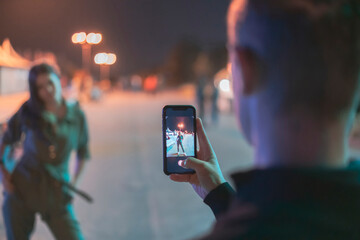 man taking a photo of a woman girlfriend using a phone in the night street
