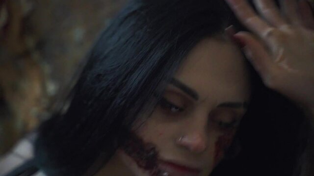 Scary Halloween makeup on the face of a young woman with black hair. Bloody wounds and lenses in the eyes