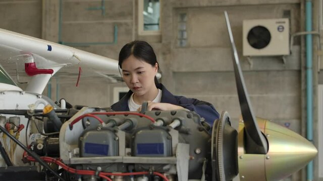 Young asian female aviation maintenance engineer doing a pre flight checkup or maintenance on a small engine aircraft in hangar. Transportation and Technology concept.