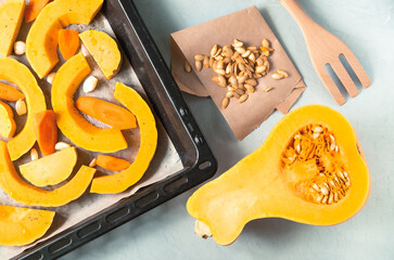 Half ripe pumpkin with seeds, pumpkin and carrot slices on a baking sheet. Healthy food concept. Horizontal orientation, selective focus, top view.