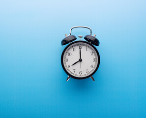 Black retro alarm clock top view, isolated on blue background. Time and morning concept