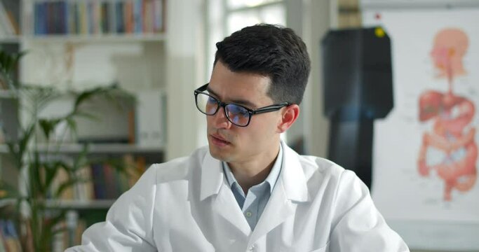Crop view of male doctor holding x ray photo while having online medical consultation in office. Man in glasses and white rob communicating with patient and looking to camera