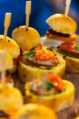 Small burgers, sliced bread and pork bologna on wooden cutting board.