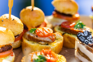 Small burgers, sliced bread and pork bologna on wooden cutting board.
