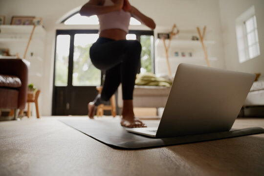Closeup of laptop on fitness mat with young woman practising yoga exercise with help of online video
