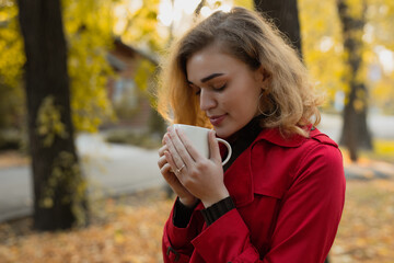 Woman sniff aroma of coffee at the fall day in park - obrazy, fototapety, plakaty