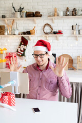 Happy young man in santa hat greeting his friends in video chat or call on tablet