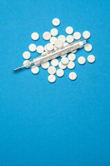 Fototapeta na wymiar group of white pills or tablets and mercury thermometer on blue background