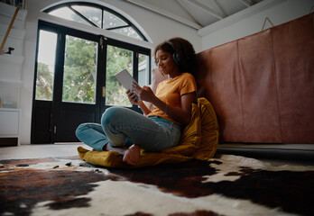 Low angle view of happy woman on carpet watching video on digital tablet and listening to music on...