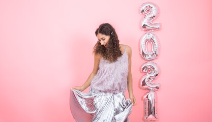 Young woman on a pink background with silver balls in the form of the numbers 2021