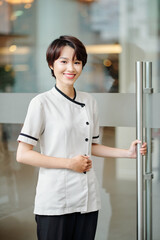 Portrait of cheerful young Asian hotel concierge opening door of boutique hotel