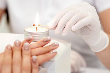 Fototapeta na wymiar Manicure master in white gloves lighting candle with match in nail salon