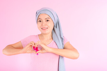 Muslim woman wearing a hijab with a ribbon on her chest shows prevention of breast cancer. On a pink backdrop, breast cancer concept, cancer prevention concept.