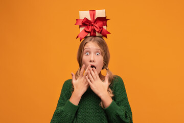 Charming blonde teen hold gift box on her head. Studio shot, yellow background. New Year Birthday Holiday concept