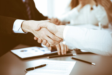 Business people shaking hands at meeting while theirs colleagues clapping and applauding. Group of unknown businessmen and women in modern white office. Success teamwork, partnership and handshake