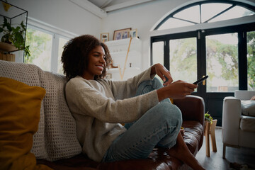 Smiling young woman relaxing on couch at home holding tv remote control
