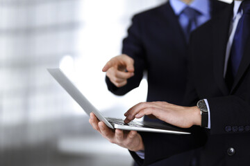 Business people discussing a presentation at meeting, standing in a modern office. Unknown businessman with a colleague search for some information at the laptop, lawyers at negotiation. Teamwork and
