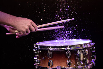 Fototapeta na wymiar Drum sticks hitting snare drum with splashing water on black background under studio lighting.