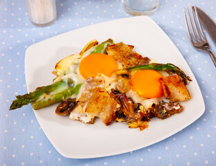 Fried eggs with sliced bacon, mushrooms and green asparagus. Hearty paleo breakfast