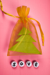yellow satin bag with a piece of green paper of Christmas Tree on a pink background. accept gifts concept