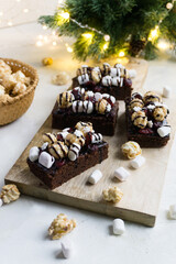 Fototapeta premium Christmas brownies decorated with chocolate, snowflakes, cranberries, marshmallows and popcorn. Christmas dessert.