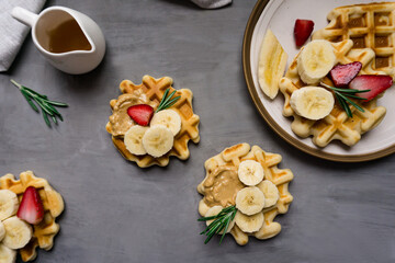 Belgian breakfast waffles with strawberries, peanut butter, banana and syrup lie on a concrete background.