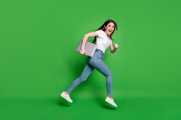 Fototapeta na wymiar Full body profile side photo of girl jump run hold laptop wear jeans t-shirt isolated over green color background