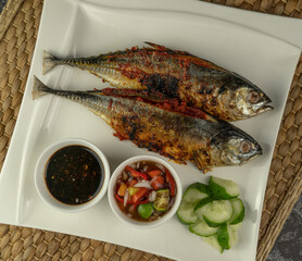 Grilled Torpedo Scad fish (Ikan Cencaru Bakar in Malay) with hot soy sauce, hot tamarind juice and fresh cucumber on white plate