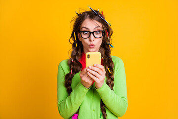 Amazed girl with pencil haircut read information on smartphone isolated over yellow color background