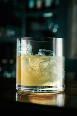 Alcoholic yellow cocktail with ice in a beautiful glass on a wooden board. Cocktail drink on the background of the bar. Selective focus