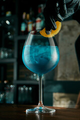 The bartender prepares an alcoholic cocktail. Decorating the drink with fruits and flowers. Blue cocktail in the beautiful glass at a bar the stands