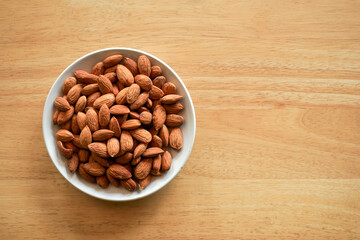 flat lay view of almond nuts in white dish on wood table with copy space
