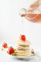 Stack of pancakes with strawberry and maple syrup.