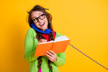 Close-up portrait of attractive funky cheerful girl talking on phone writing home task discussing isolated bright yellow color background