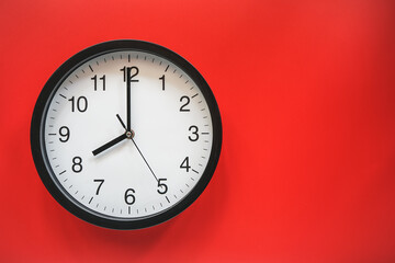 Classic black and white analog clock on red background at Eight o'clock with copy space