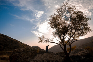 Obraz premium People and kids enjoying a beautiful warm yellow sunset on a green field and the trees in front of the sun in the mountains in algeria