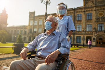 Old man in mask while sitting in wheelchair in yard