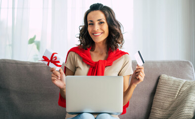 Beautiful happy young woman in casual clothes is sitting on the couch at home and doing online shopping on black friday.