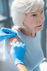 Elderly grey-haired woman having vaccination and looking serious